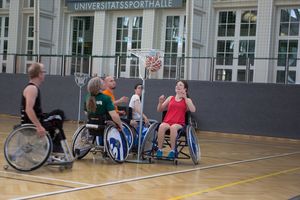 In der Sporthalle: Zwei Frauen und drei Männer in Rollstühlen scharen sich um einen Basketball-Korb, in den gerade ein Ball hinein fällt. © Hildegardis-Verein/Agathe Lukassek
